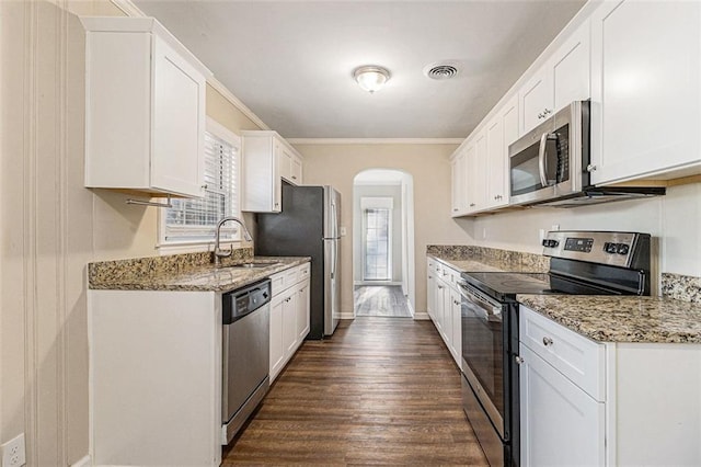 kitchen featuring sink, light stone counters, appliances with stainless steel finishes, white cabinets, and ornamental molding