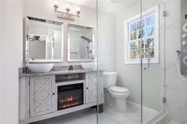 bathroom featuring toilet, a sink, marble finish floor, a shower stall, and double vanity