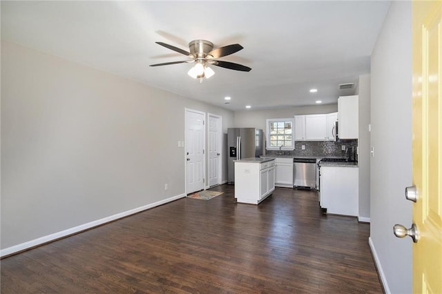 kitchen featuring dark wood-style flooring, backsplash, appliances with stainless steel finishes, a kitchen island, and baseboards