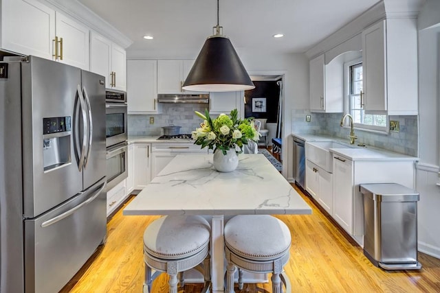 kitchen featuring stainless steel appliances, a kitchen island, sink, and decorative light fixtures