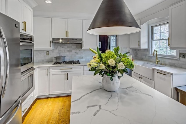 kitchen with sink, white cabinetry, backsplash, stainless steel appliances, and light stone counters