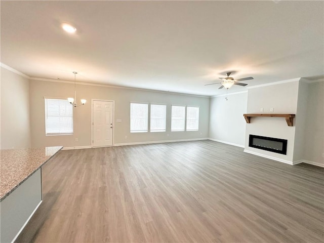 unfurnished living room featuring ceiling fan with notable chandelier, a glass covered fireplace, light wood-style floors, crown molding, and baseboards