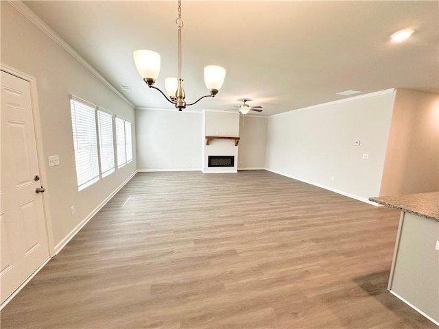 unfurnished living room with light wood finished floors, ceiling fan with notable chandelier, a fireplace, and crown molding