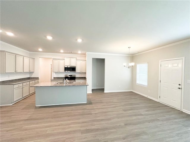 kitchen with light wood-type flooring, a notable chandelier, a kitchen island with sink, ornamental molding, and stainless steel microwave