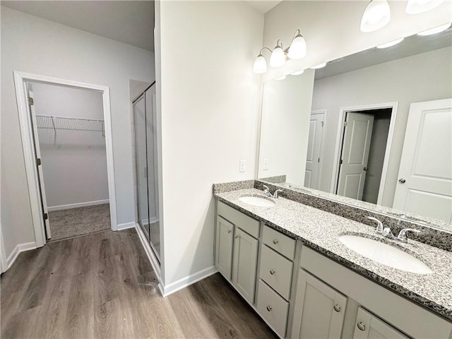 full bath featuring double vanity, a stall shower, a walk in closet, and a sink