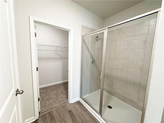 full bathroom with a walk in closet, baseboards, wood finished floors, and a shower stall