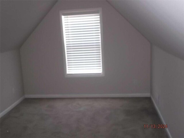 bonus room with dark carpet and vaulted ceiling