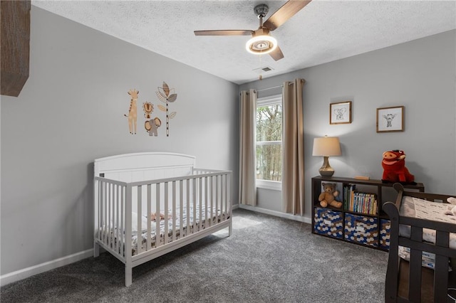 carpeted bedroom with a crib, visible vents, baseboards, ceiling fan, and a textured ceiling