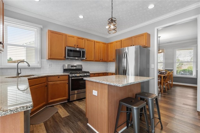 kitchen featuring a kitchen island, ornamental molding, dark wood-type flooring, stainless steel appliances, and a sink