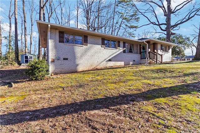 view of front of property with an outbuilding, brick siding, a front yard, crawl space, and a shed