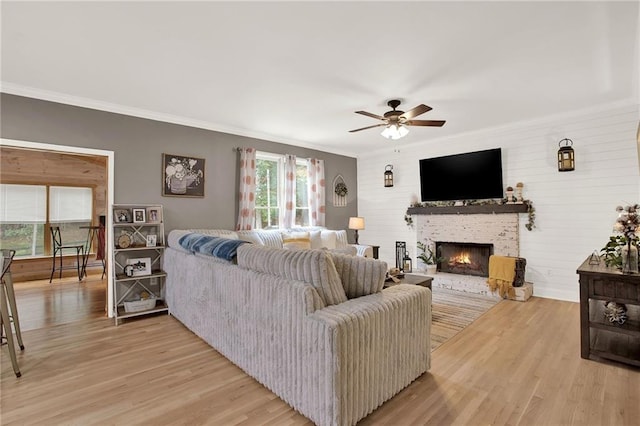 living room with hardwood / wood-style floors, a stone fireplace, ceiling fan, and crown molding