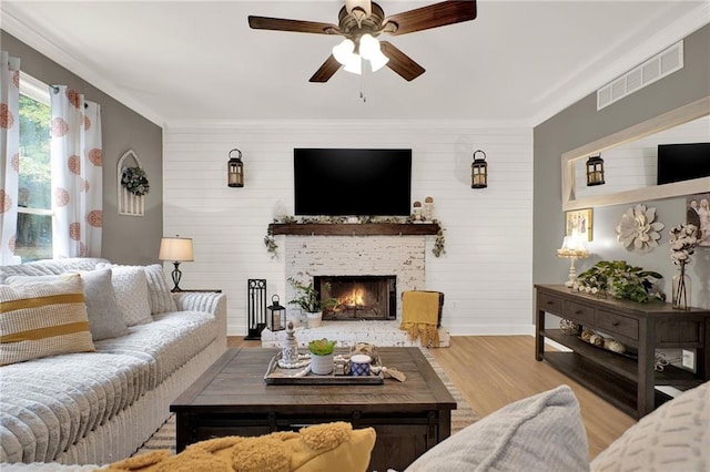 living room featuring light wood-type flooring, ornamental molding, ceiling fan, a fireplace, and wood walls