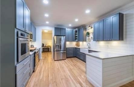 kitchen featuring backsplash, stainless steel appliances, blue cabinets, and light hardwood / wood-style floors