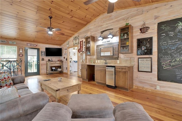 living room with ceiling fan, vaulted ceiling with beams, light hardwood / wood-style flooring, wood walls, and wood ceiling