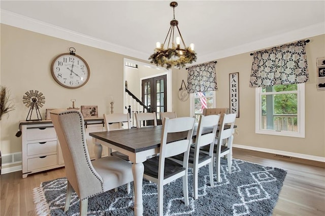 dining space with a notable chandelier, light wood-type flooring, crown molding, and french doors