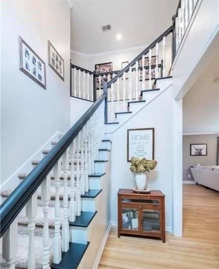 stairs with a towering ceiling, hardwood / wood-style flooring, and ornamental molding