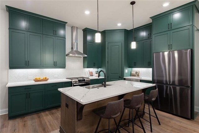 kitchen featuring pendant lighting, wall chimney range hood, sink, appliances with stainless steel finishes, and light stone countertops