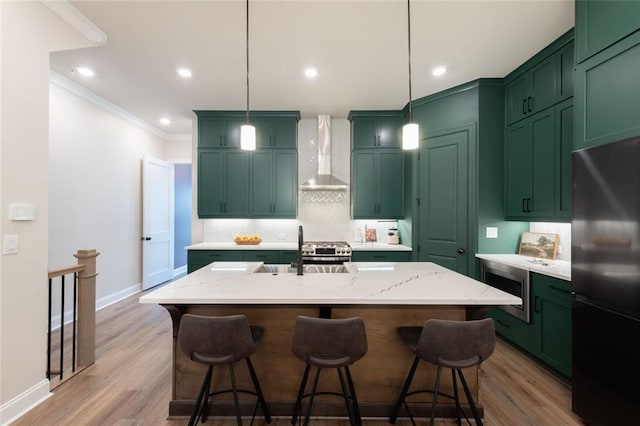 kitchen featuring pendant lighting, refrigerator, light stone countertops, a center island with sink, and wall chimney exhaust hood