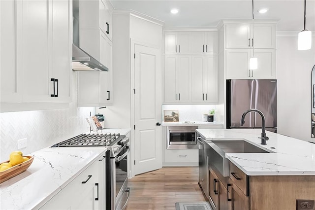 kitchen with pendant lighting, wall chimney exhaust hood, white cabinets, and appliances with stainless steel finishes