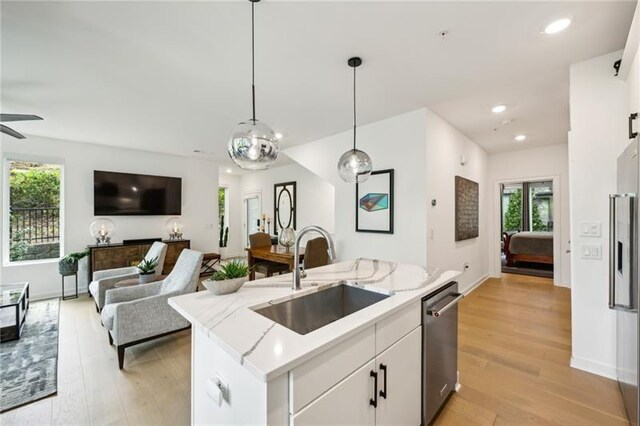 kitchen featuring white cabinetry, sink, stainless steel appliances, an island with sink, and decorative light fixtures