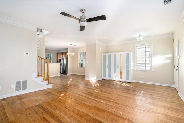 unfurnished living room with ceiling fan with notable chandelier, light hardwood / wood-style flooring, and ornamental molding