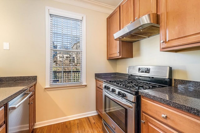 kitchen featuring dark stone counters, stainless steel appliances, light wood-type flooring, and ornamental molding