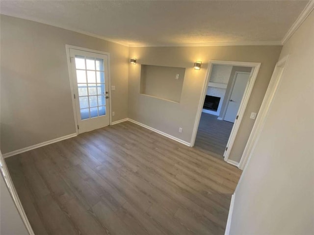 spare room with wood-type flooring, a brick fireplace, and crown molding