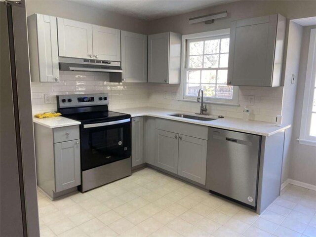 kitchen with stainless steel appliances, gray cabinets, sink, and decorative backsplash