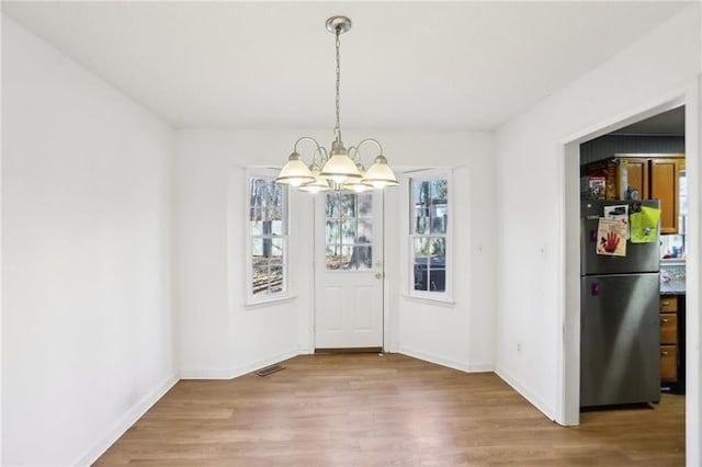 unfurnished dining area with hardwood / wood-style flooring, a healthy amount of sunlight, and a chandelier