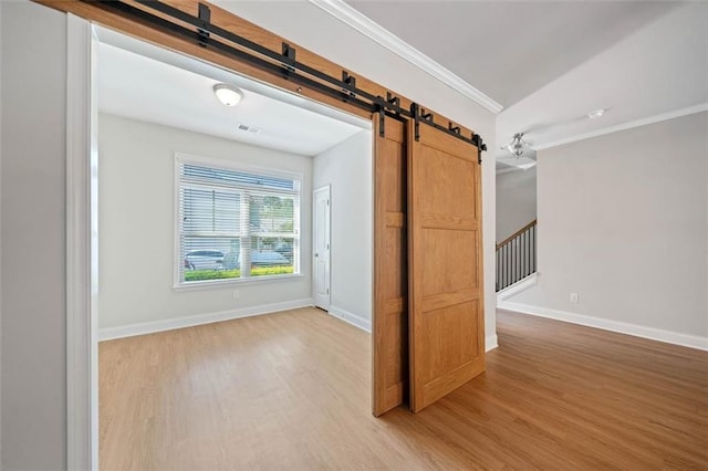 empty room with visible vents, crown molding, light wood-style floors, and a barn door