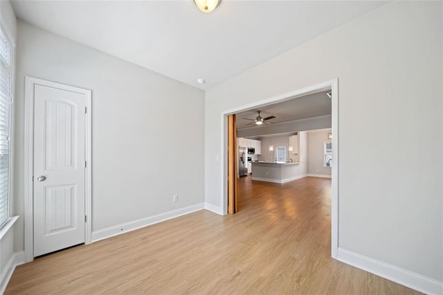 spare room featuring a ceiling fan, baseboards, and light wood finished floors