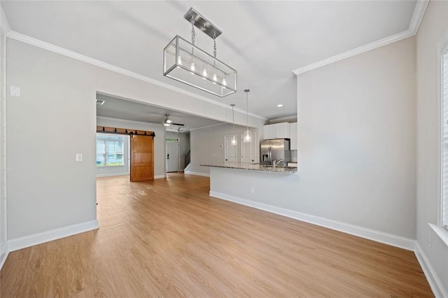 unfurnished living room with a barn door, baseboards, light wood-type flooring, and ornamental molding