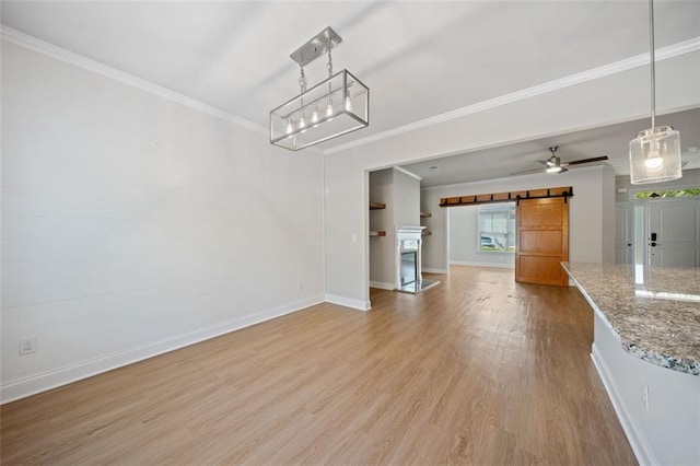 unfurnished dining area featuring ornamental molding, a barn door, light wood-style floors, baseboards, and ceiling fan