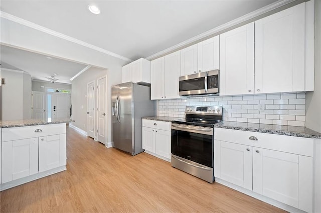 kitchen featuring crown molding, dark stone counters, light wood-type flooring, appliances with stainless steel finishes, and white cabinetry