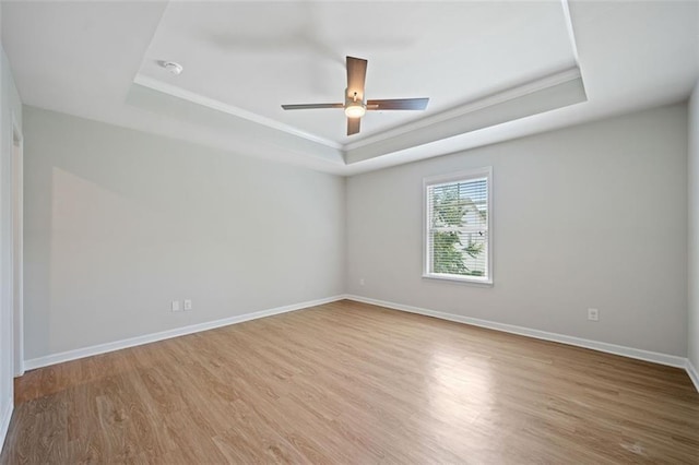 spare room featuring a tray ceiling, baseboards, and wood finished floors