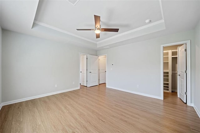 unfurnished bedroom featuring a walk in closet, a raised ceiling, baseboards, and light wood finished floors