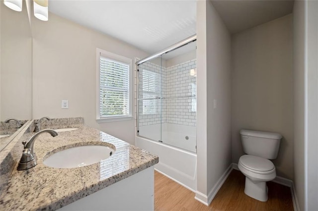 bathroom with wood finished floors, shower / bath combination with glass door, toilet, and a sink