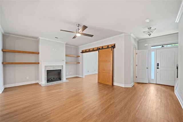 unfurnished living room featuring a barn door, baseboards, ornamental molding, and light wood finished floors