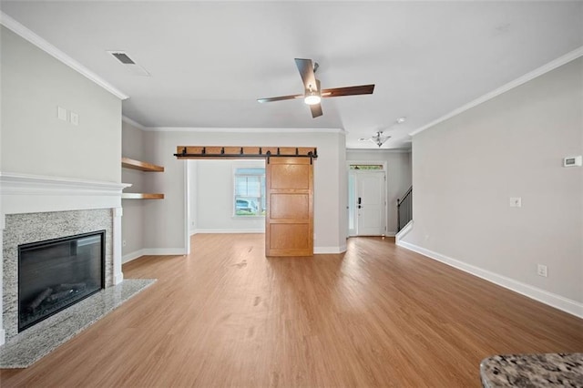 unfurnished living room with a ceiling fan, baseboards, light wood finished floors, a glass covered fireplace, and crown molding