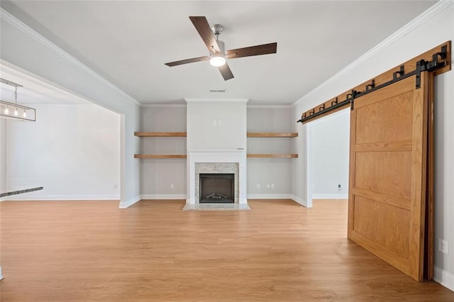 unfurnished living room featuring visible vents, light wood finished floors, a fireplace with flush hearth, ornamental molding, and a barn door