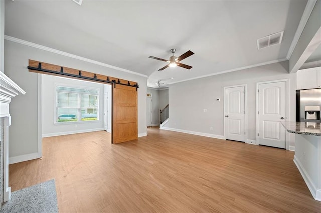 unfurnished living room featuring visible vents, ceiling fan, a barn door, and ornamental molding