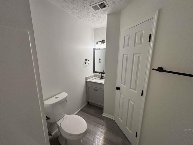 bathroom with vanity, wood finished floors, visible vents, a textured ceiling, and toilet