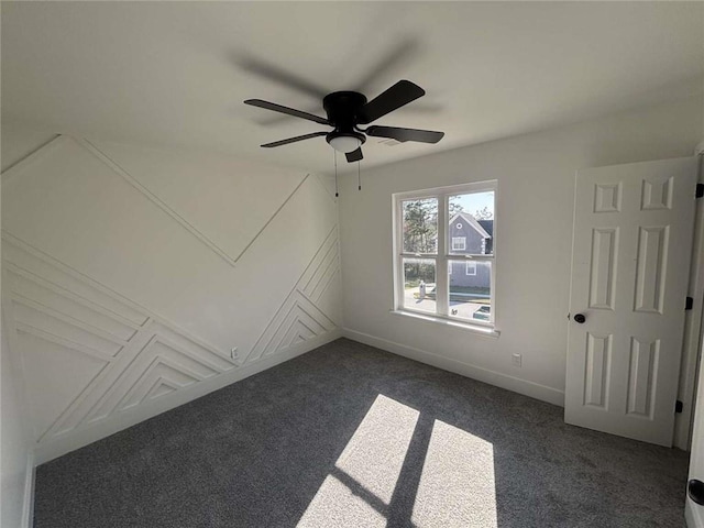 empty room featuring attic access, dark carpet, baseboards, and ceiling fan