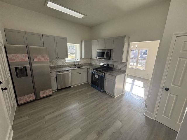 kitchen with tasteful backsplash, gray cabinetry, appliances with stainless steel finishes, wood finished floors, and a sink