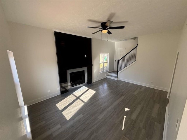 unfurnished living room featuring stairway, a textured ceiling, ceiling fan, and dark wood-style flooring