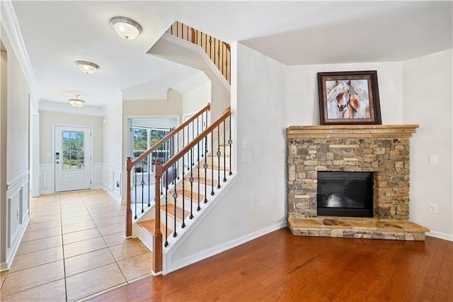 foyer with wood finished floors, a stone fireplace, a decorative wall, crown molding, and stairs