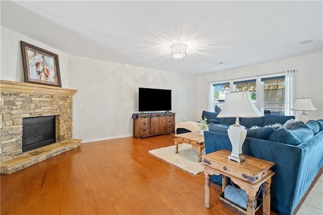 living area featuring light wood-style floors, a stone fireplace, and baseboards