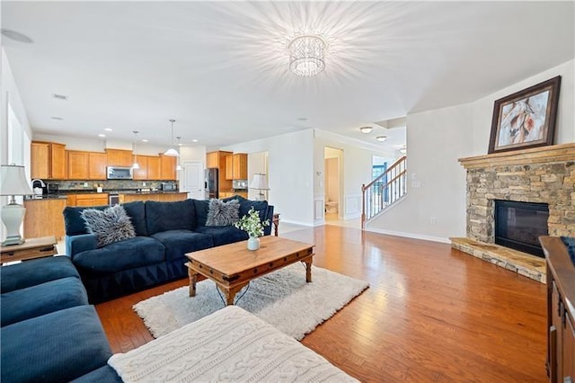 living area with stairway, an inviting chandelier, baseboards, a fireplace, and light wood-style flooring