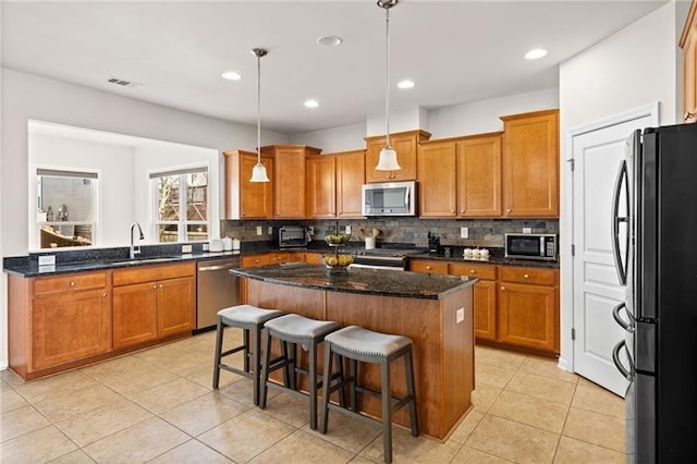 kitchen with a center island, a sink, decorative backsplash, brown cabinetry, and appliances with stainless steel finishes