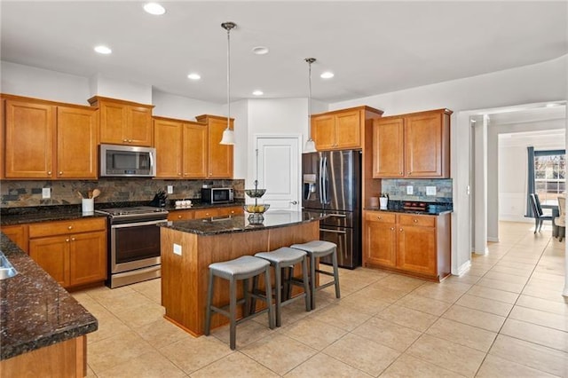 kitchen featuring stainless steel appliances, dark stone countertops, backsplash, brown cabinetry, and a kitchen island